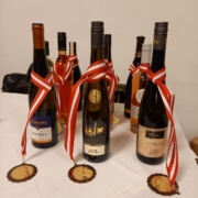 Das Bild zeigt Preise für die Gewinner der Honigprämierung. Zu sehen sind 6 Weinflaschen. Um jede Flasch ist eine Medaille gehängt.