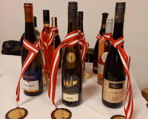 Das Bild zeigt Preise für die Gewinner der Honigprämierung. Zu sehen sind 6 Weinflaschen. Um jede Flasch ist eine Medaille gehängt.